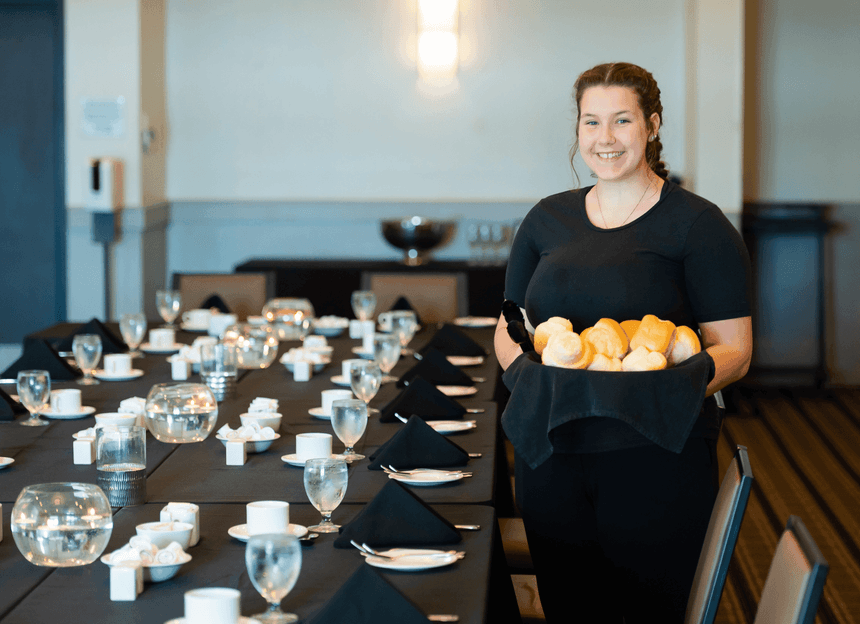 Server holding bread by a long banquet table at Rodd Hotels & Resorts, one of the best hotels in Charlottetown, PEI hotel