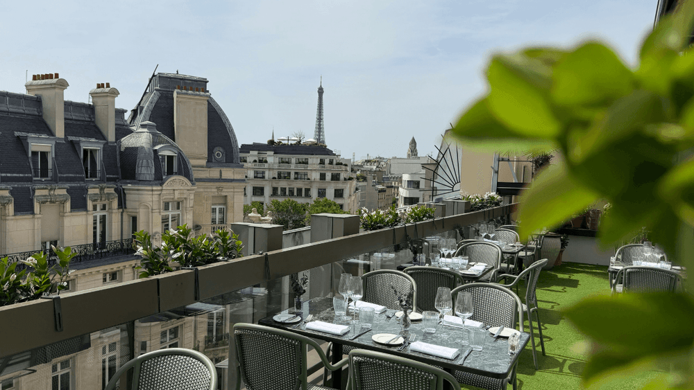 Terrasse parisienne avec vue sur la Tour Eiffel et tables dressées entourées de verdure luxuriante