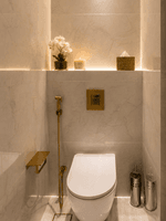 Bidet sprayer and gold flush plate on marble wall above toilet in Deluxe Skyline View at Naviti by Warwick Jeddah
