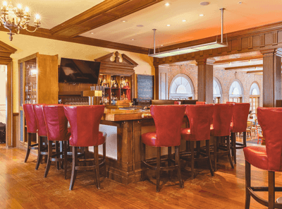 Wide shot of the bar counter with bar shelves and plush seating in Epoch Restaurant & Bar at The Exeter Inn