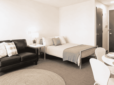 Modern studio apartment with bed, black leather sofa, dining table, and neutral decor at Student Living - Waymouth