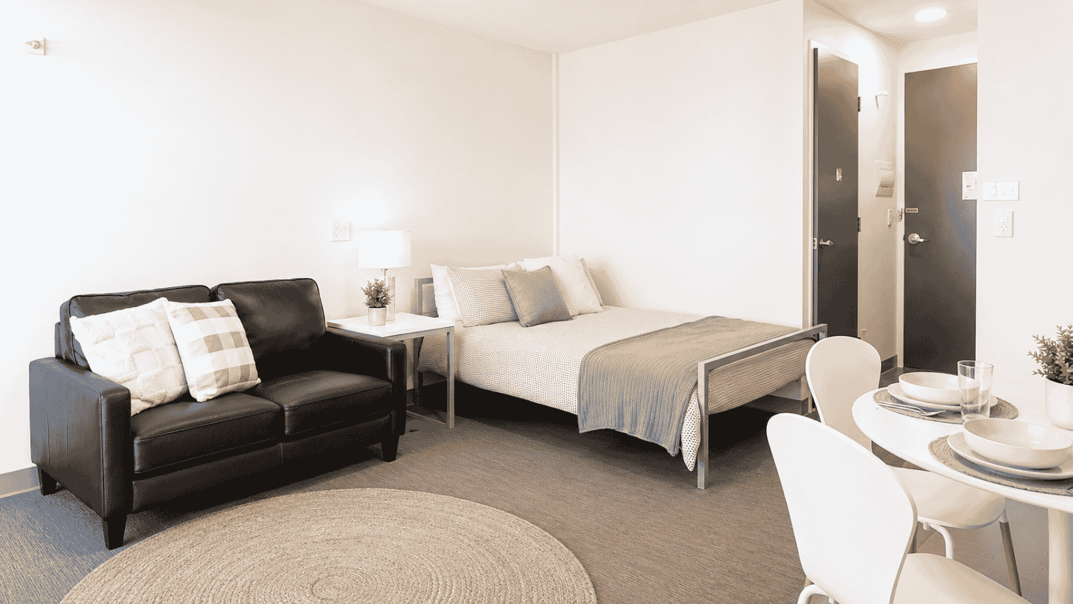 Modern studio apartment with bed, black leather sofa, dining table, and neutral decor at Student Living - Waymouth