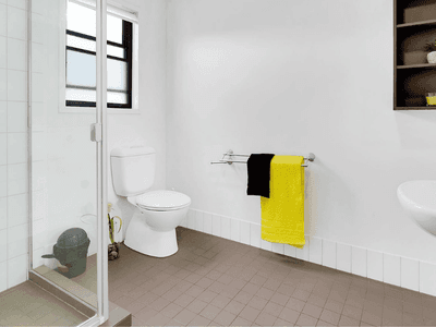Modern bathroom with white walls, glass shower, toilet, wall-mounted sink, and bright yellow towel at Springfield Central.