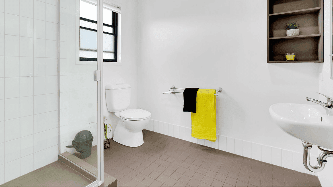 Modern bathroom with white walls, glass shower, toilet, wall-mounted sink, and bright yellow towel at Springfield Central.