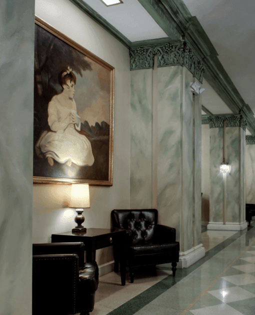 Elegant hallway at Knickerbocker On The Lake featuring a classic portrait, leather chairs, and marble floors