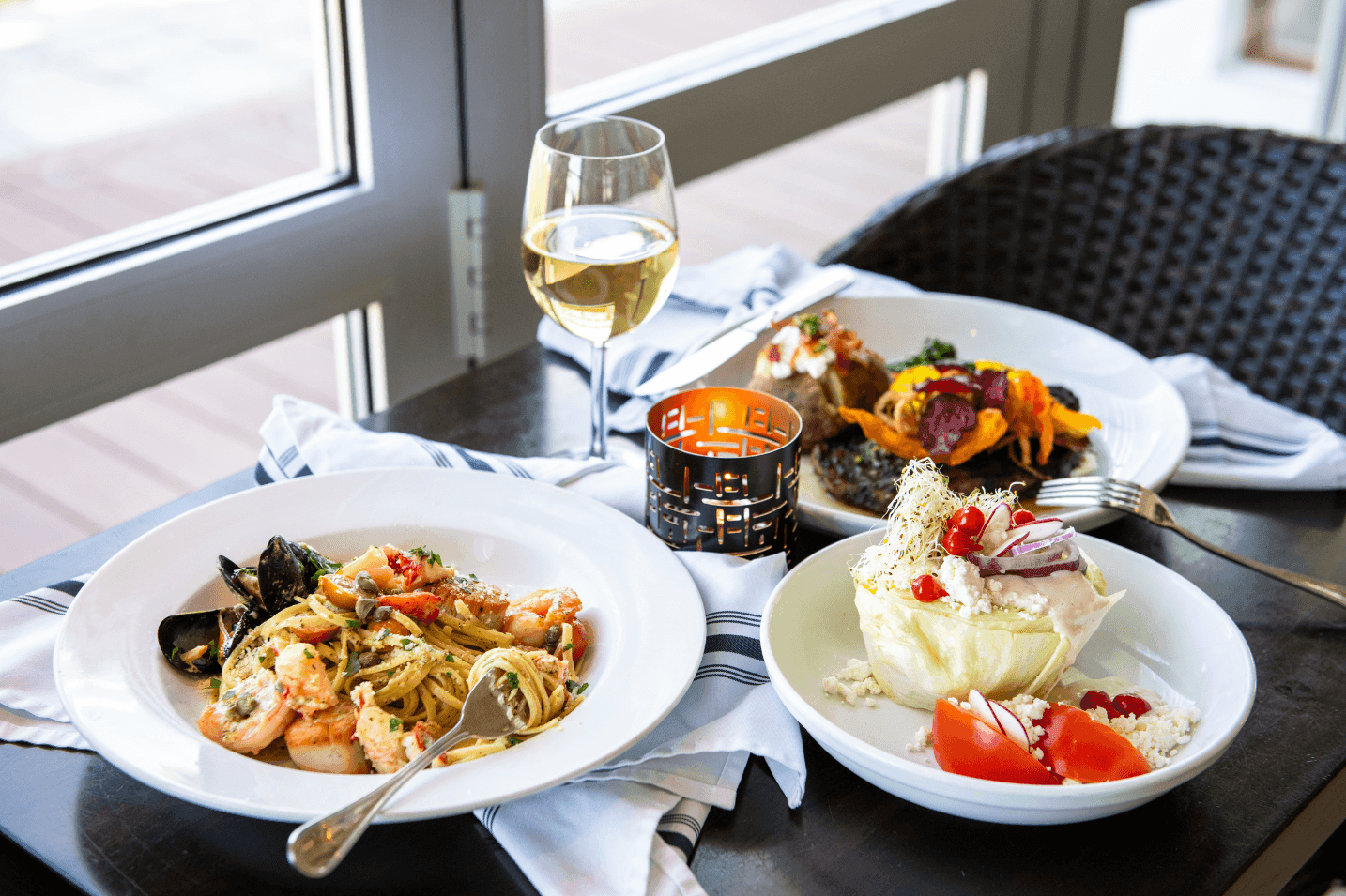 A table set with three plates of food, a glass of wine, and a candle.