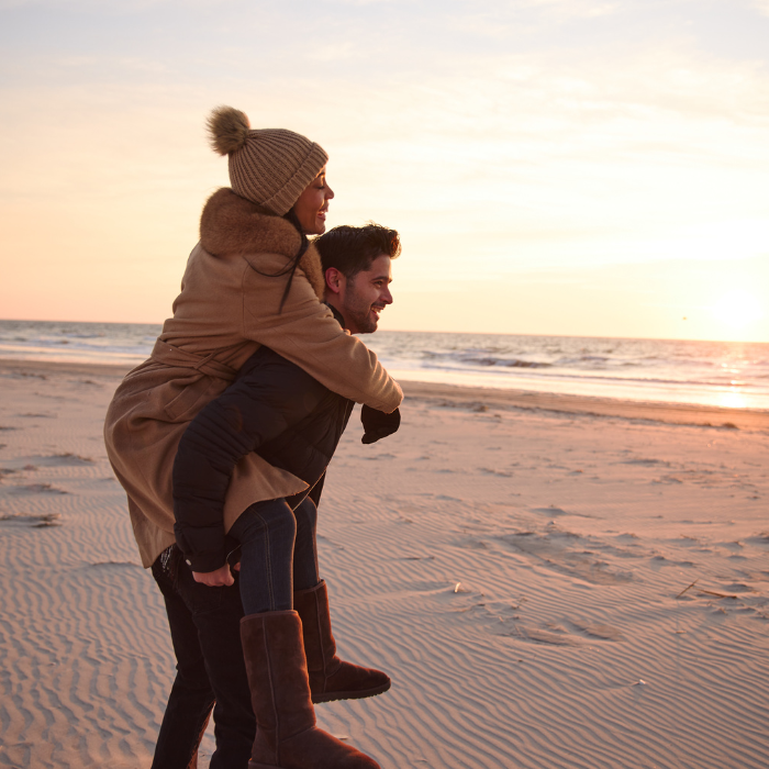 Young couple in winter clothes riding piggy back on the beach watching the sunrise at ICONA Avalon resort in Avalon NJ