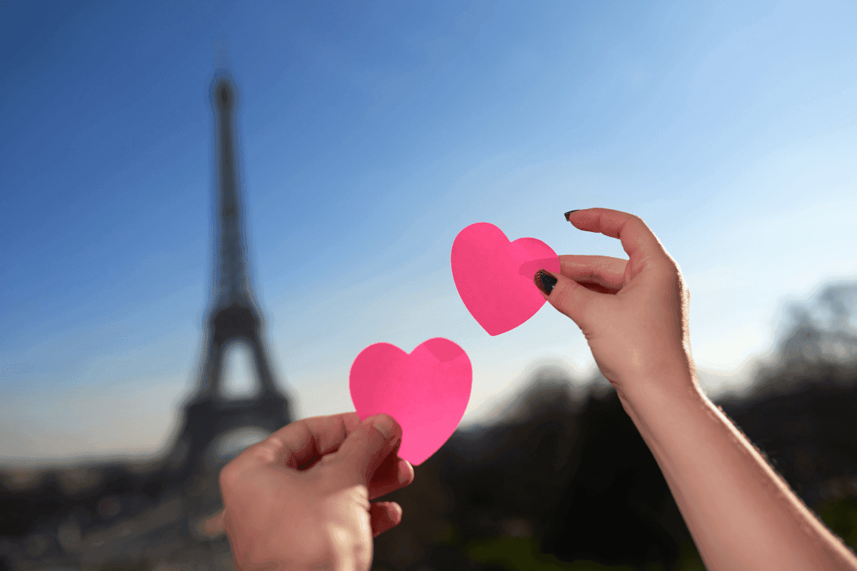 Hands holding paper hearts by the Eiffel Tower under a bright sky near Warwick Paris Champs Elysées