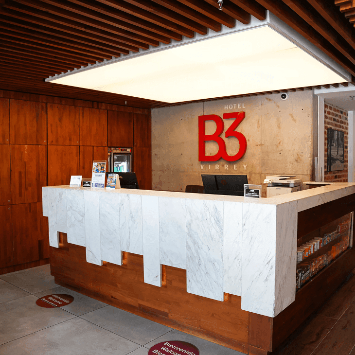 Mostrador de recepción con paneles de mármol blanco bajo un techo de madera en Unika Hotels, hotel de élite en Bogotá