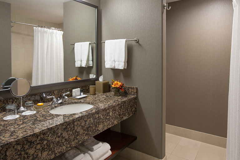A hotel bathroom with a granite countertop, large mirror, and towels.
