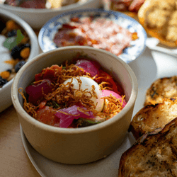 Bowl of salad with egg, bread slices, and other dishes on a table.