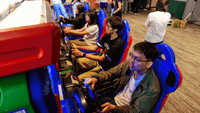 Students playing racing arcade games in a colorful gaming lounge with blue and red chairs at UniLodge.