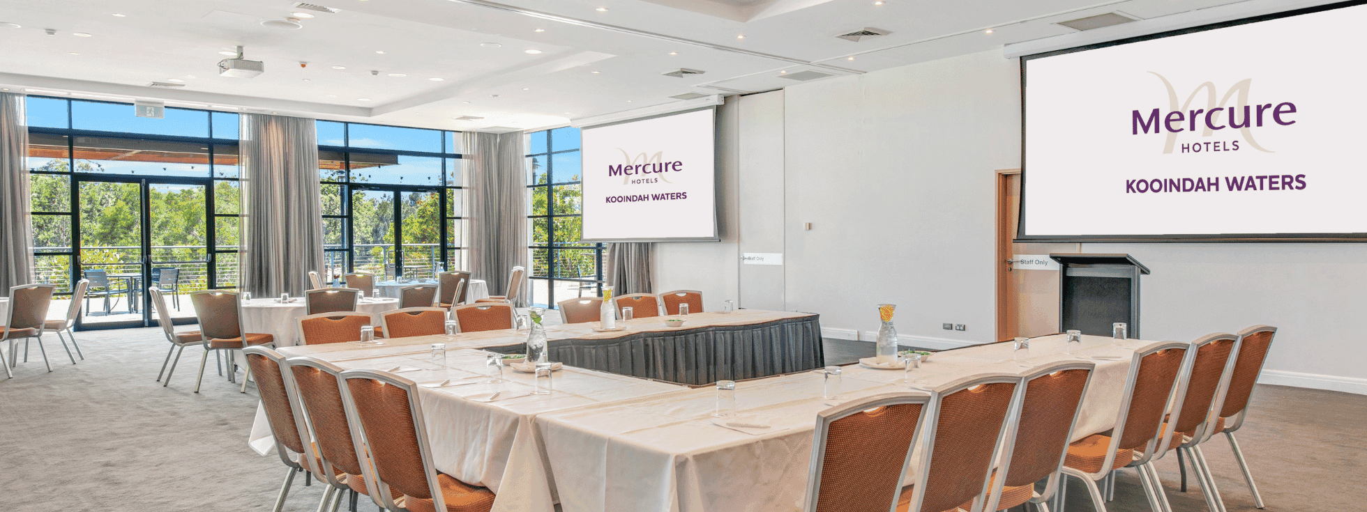 Conference room with long tables, chairs, and screens displaying 
