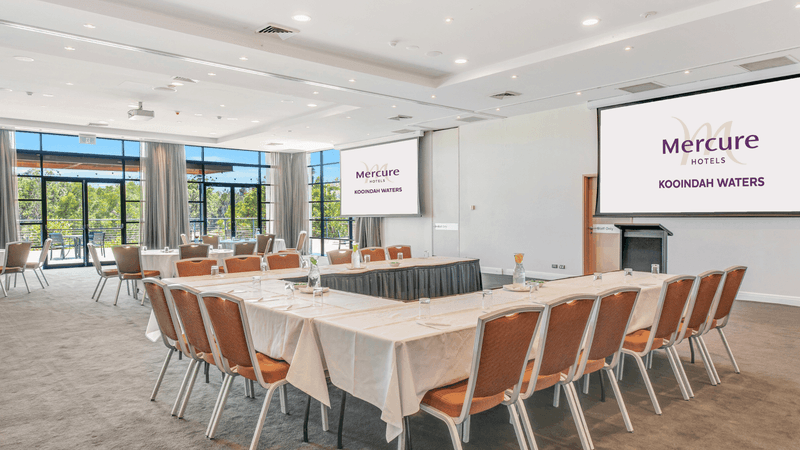 Conference room with long tables, chairs, and screens displaying 