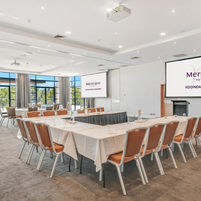 Kooindah Two Meeting room set up with tables, chairs, and a presentation screen at Mercure Kooindah Waters