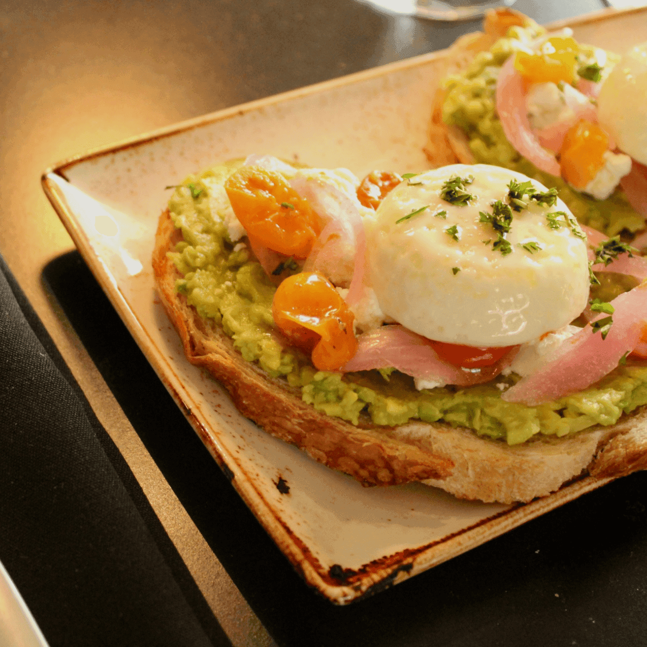 Plate of two avocado toasts with poached eggs, cherry tomatoes, and onions in Events module.