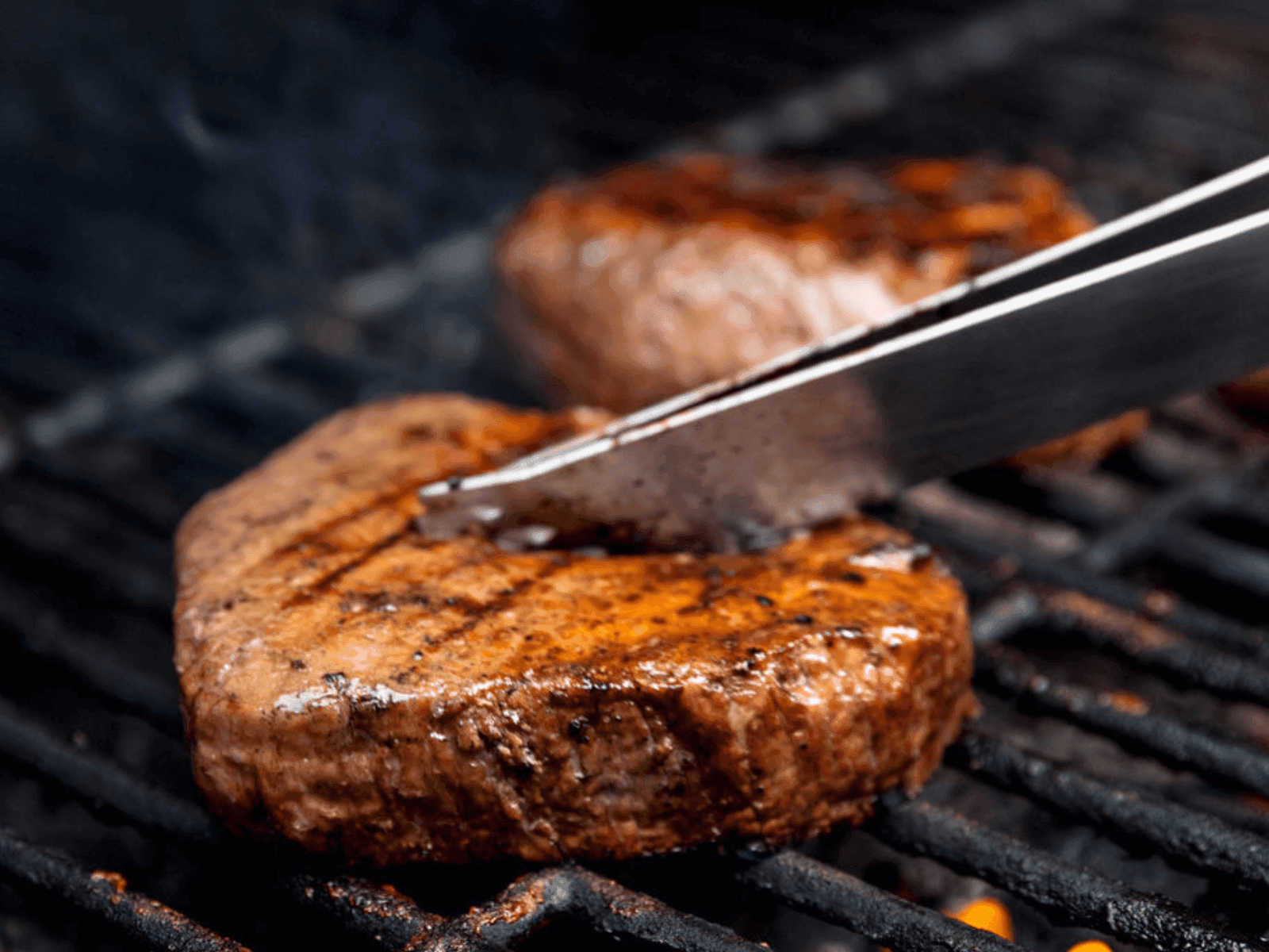 Close-up of grilling steak on BBQ with a silver tong at Blackcomb Springs Suites