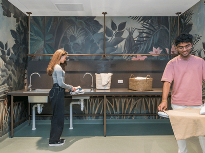 A man and a woman ironing clothes in a laundry room with a jungle-themed mural.