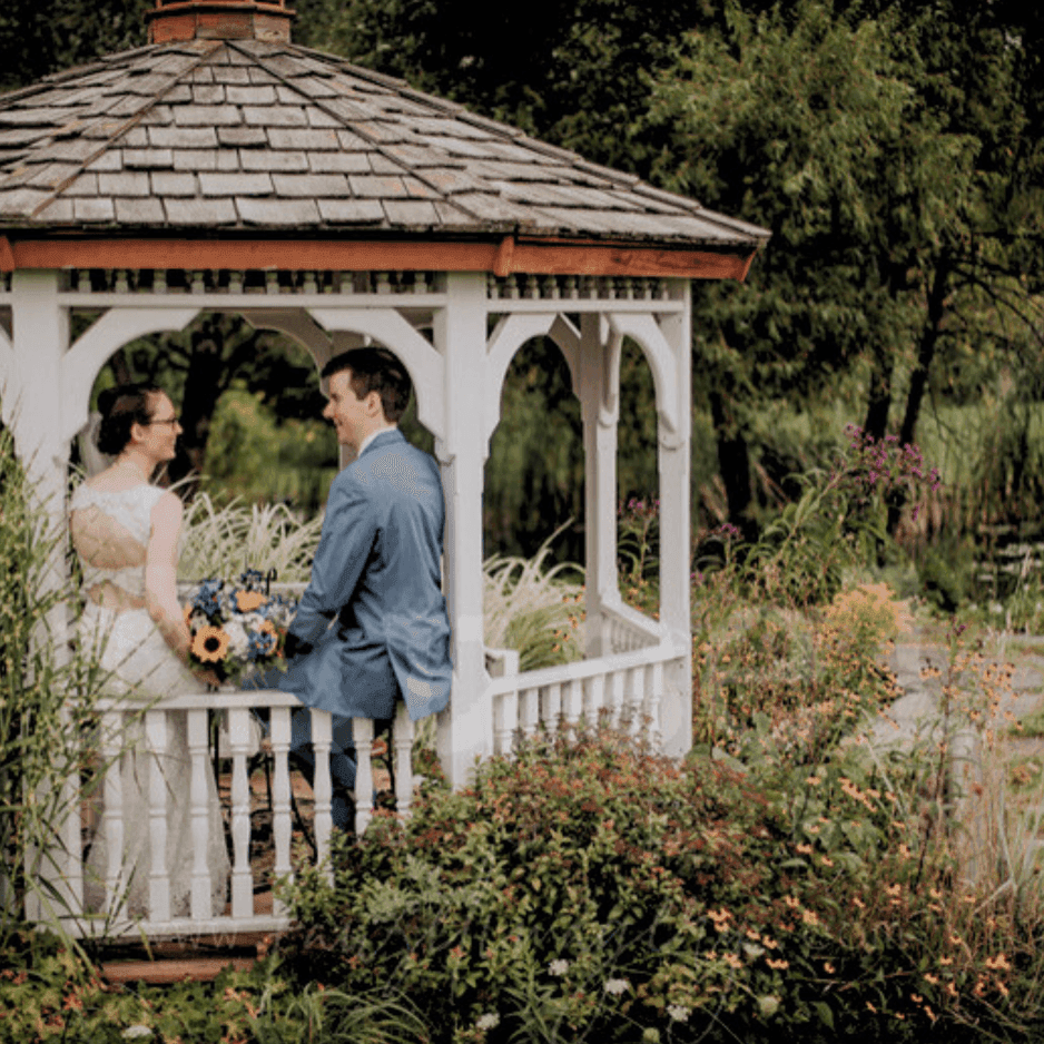 Bride and groom holding hands inside a white gazebo, surrounded by tall grasses near La Tourelle Inn and Spa