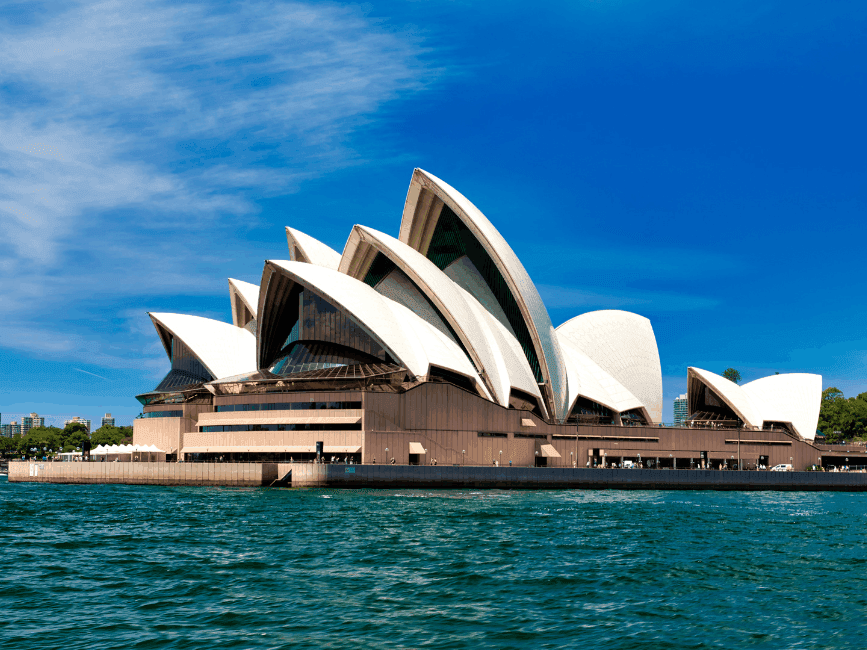 Sydney Opera House with a clear blue sky and water in front.