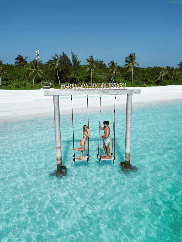 Couple on swings over the crystal blue water at Grand Park Kodhipparu