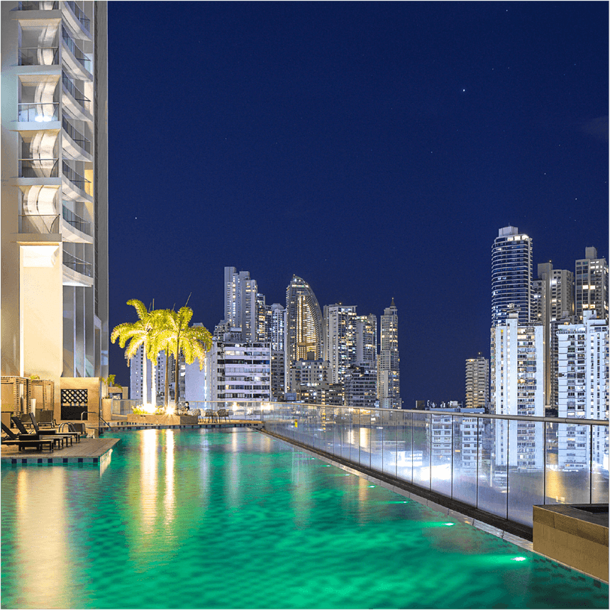 Piscina de azotea de noche con tumbonas, torre, palmeras iluminadas y vistas urbanas en Megapolis Hotel Panama