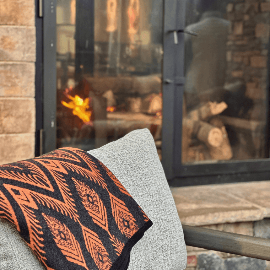 Patterned blanket folded over a gray pillow, next to a glass-enclosed fireplace at The Embers Hotel