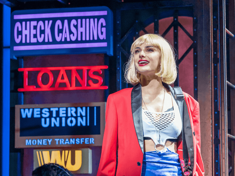 Woman in red jacket and blue skirt on stage at Pretty Woman: The Musical.