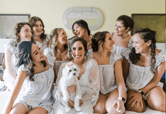 Group of bridesmaids in matching outfits with white dog sitting together indoors in Inn at Willow Grove