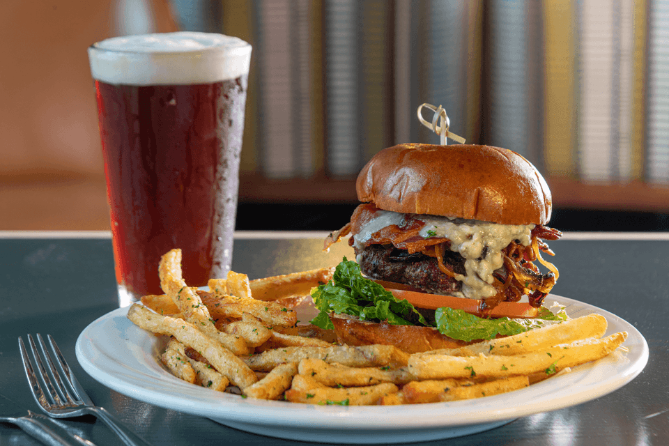Bacon cheeseburger with lettuce and tomato beside seasoned fries and a beer at La Tourelle Inn and Spa