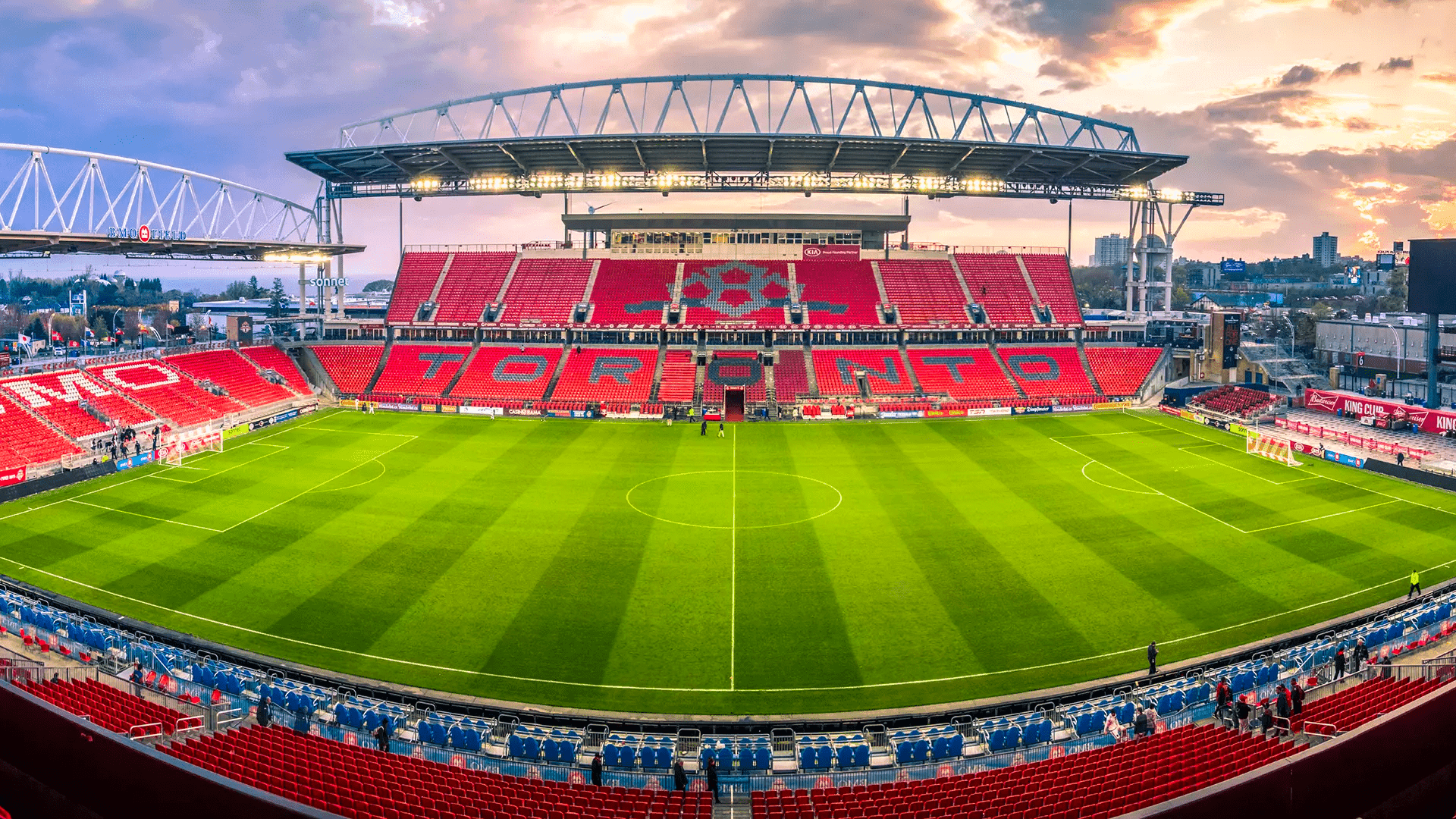 BMO Field with red seating surrounds a green soccer pitch under a curved canopy roof near Hotel X Toronto