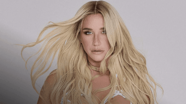 Blonde woman with long hair wearing a white top and a gold necklace.