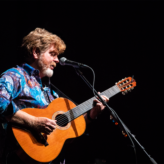 Musician Mac McAnally with an acoustic guitar and blue shirt with black background. Live Concert in Avalon NJ August 16 2022
