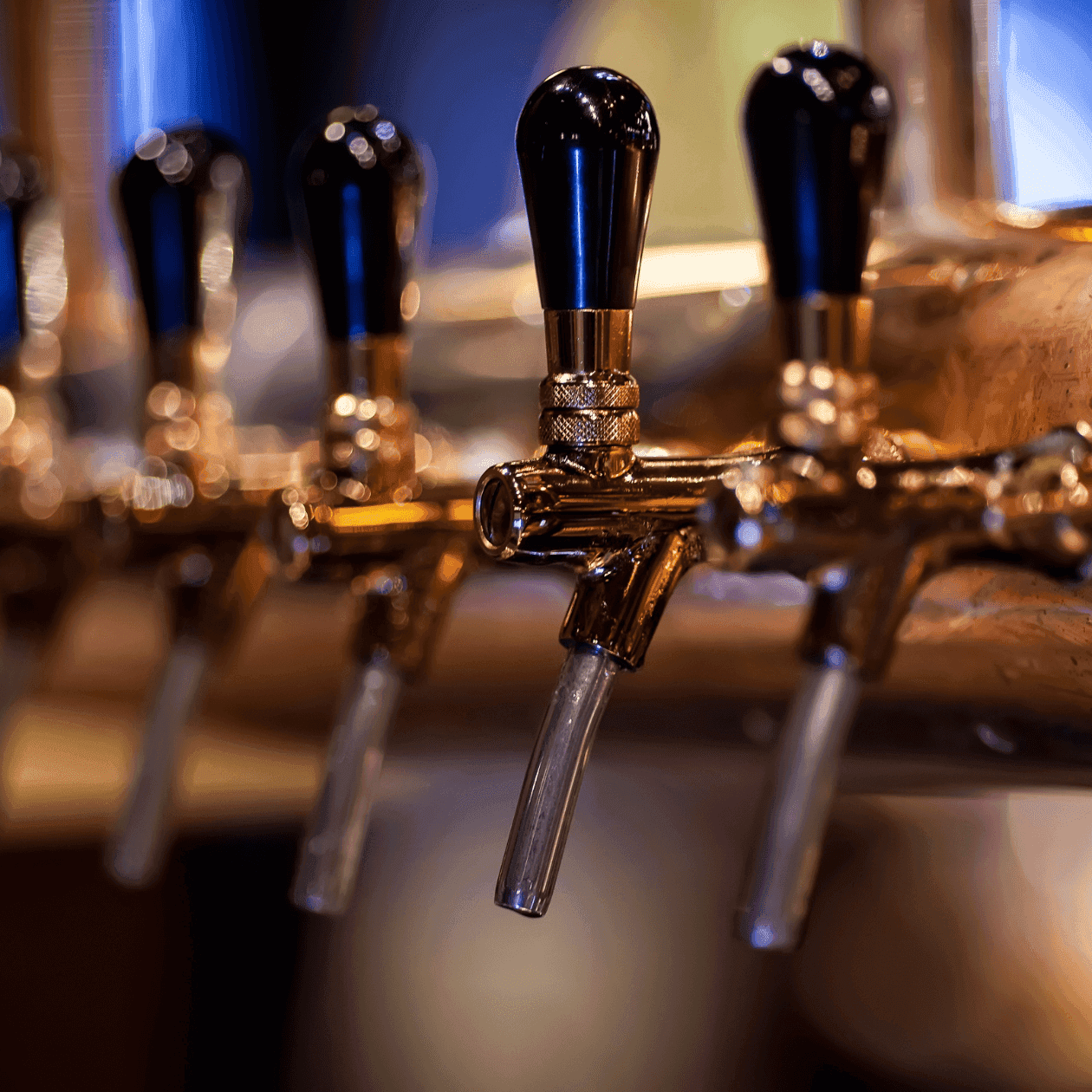 Close-up of multiple beer taps with clear tubes and black handles against a blurred background.