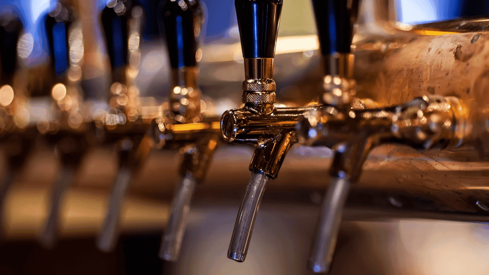 Close-up of multiple beer taps with clear tubes and black handles against a blurred background.