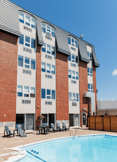 Outdoor swimming pool on a patio deck outside the brick hotel building under a clear blue sunny sky at Rodd Moncton
