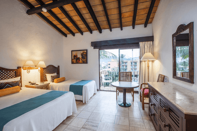 Two beds, a table, and a balcony with an outdoor view in a hotel room.