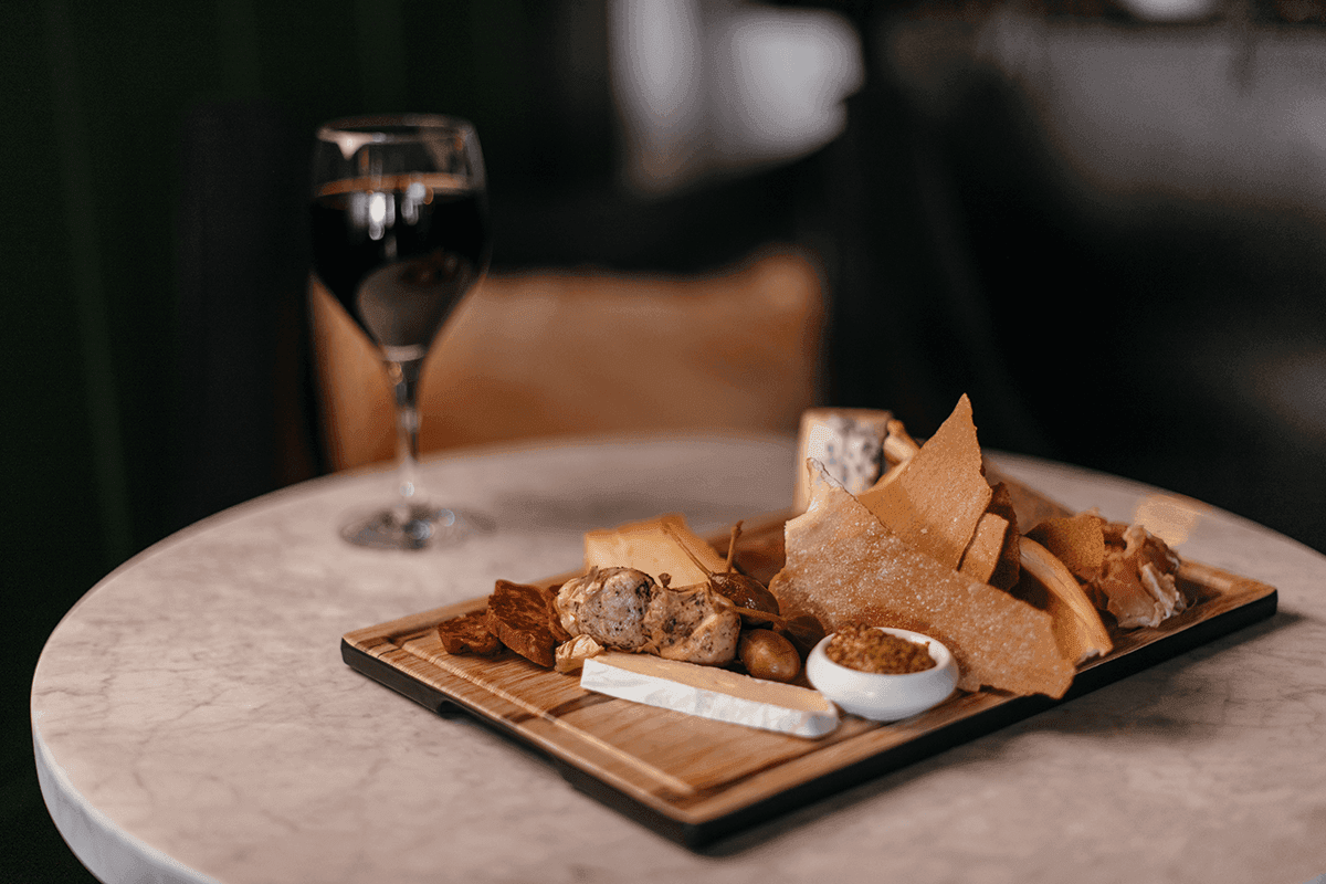 Charcuterie board with cheese and meats next to a glass of wine in 1865 Wine Cellar at Mountain View Grand Resort & Spa