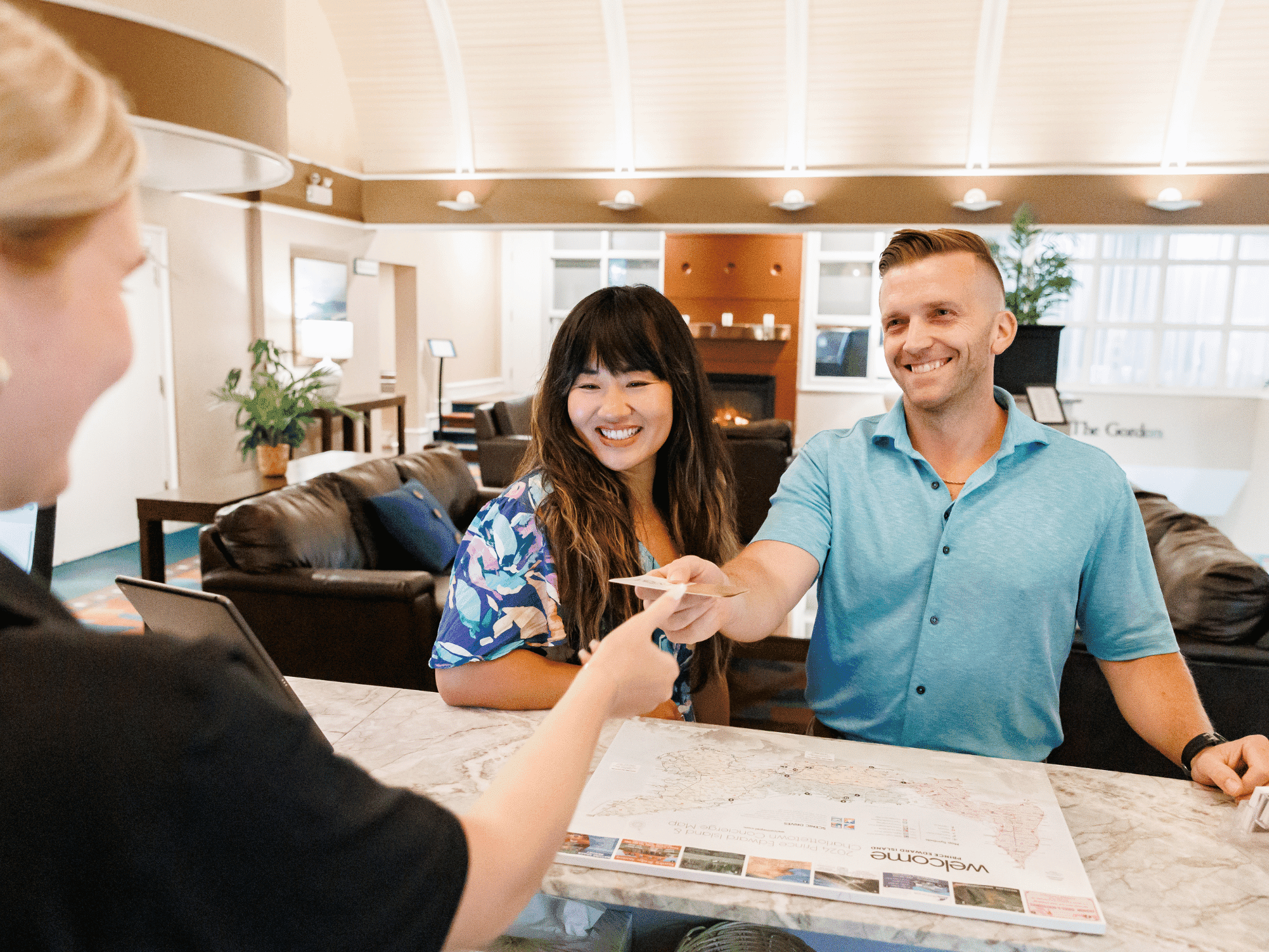 Smiling couple receiving a room key card and a map from a staff member at the Rodd Hotels & Resorts front desk