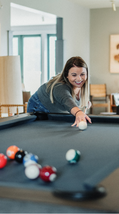 A guest lining up her shot on a pool table to sink a ball in the pocket