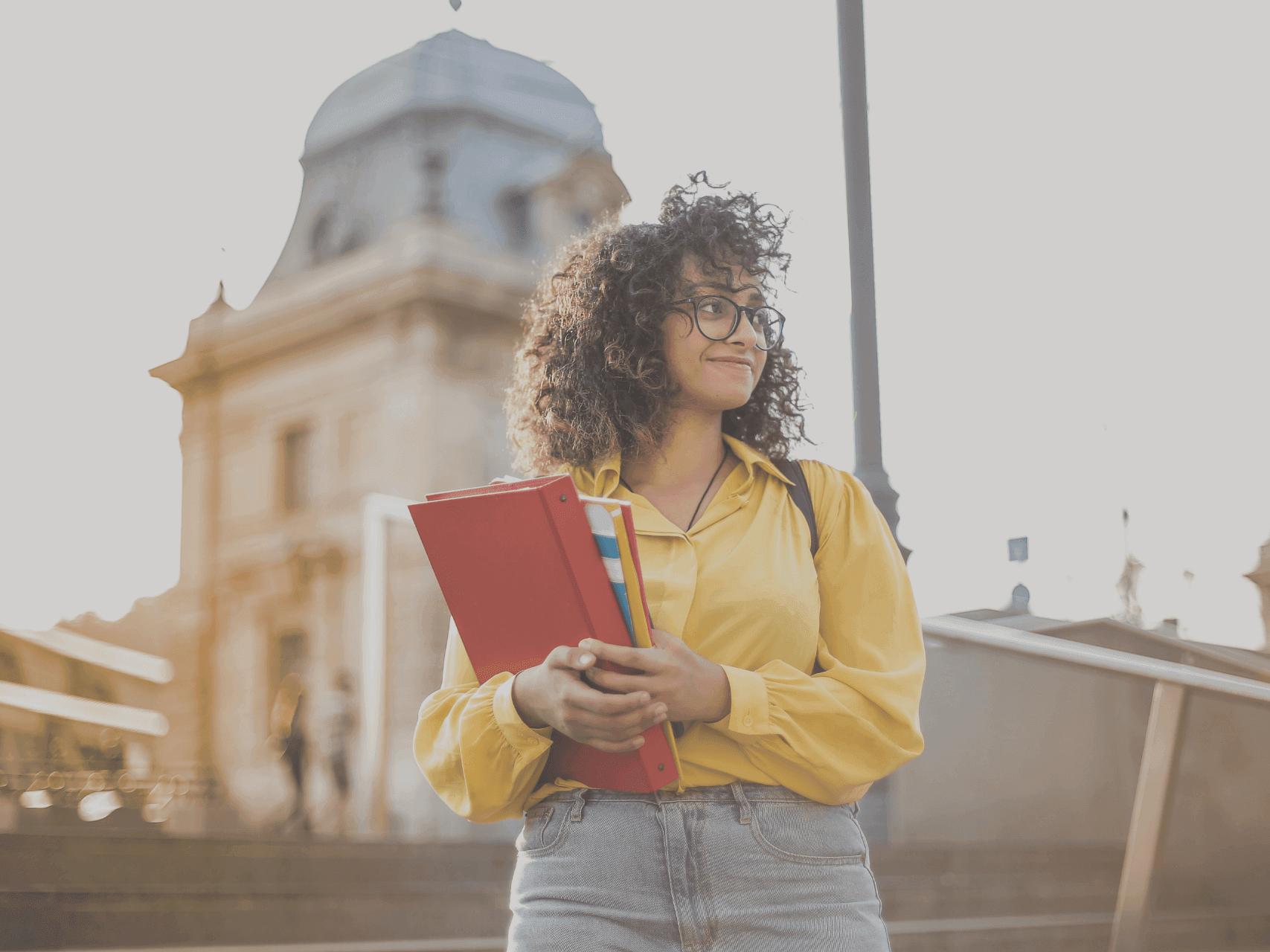 Student holding notebooks outdoors near a historic building for Back to School Savings.