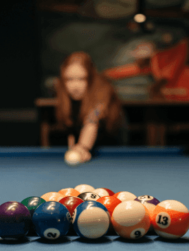 Close-up of the billiard balls on the pool table, with a lady aiming in the background at Cove Pocono Resorts