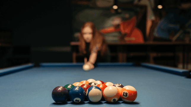 Close-up of the billiard balls on the pool table, with a lady aiming in the background at Cove Pocono Resorts