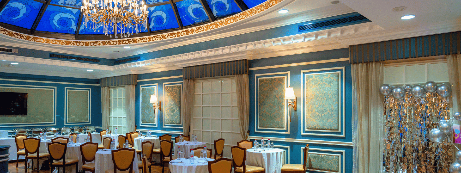 Round dining tables by yellow chairs under a blue stained-glass dome in Blue Room at Warwick Hotels & Resort