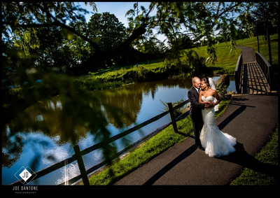 Bride and groom embrace beside a tranquil pond with a wooden bridge and landscape at Aramark Chauncey Conference Center