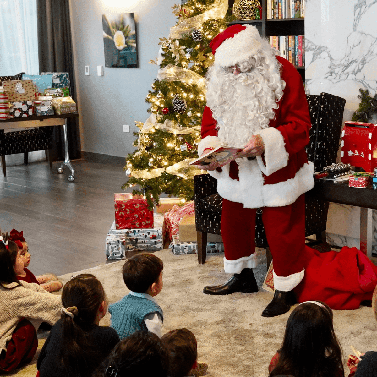 Santa reading a book to children seated by a lit Christmas tree, under warm string lights at Hotel X Toronto