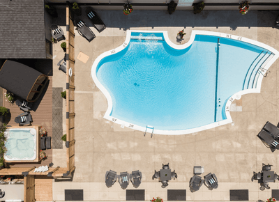 Aerial view over an outdoor swimming pool patio featuring lounge chairs and a hot tub deck under sunlight at Rodd Moncton