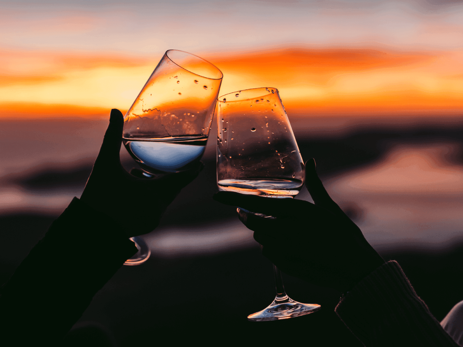 Two glasses of wine clinking at dusk