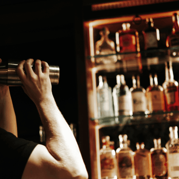 Bartender shaking a cocktail shaker beside a glowing shelf of liquor bottles at the bar at La Tourelle Inn and Spa