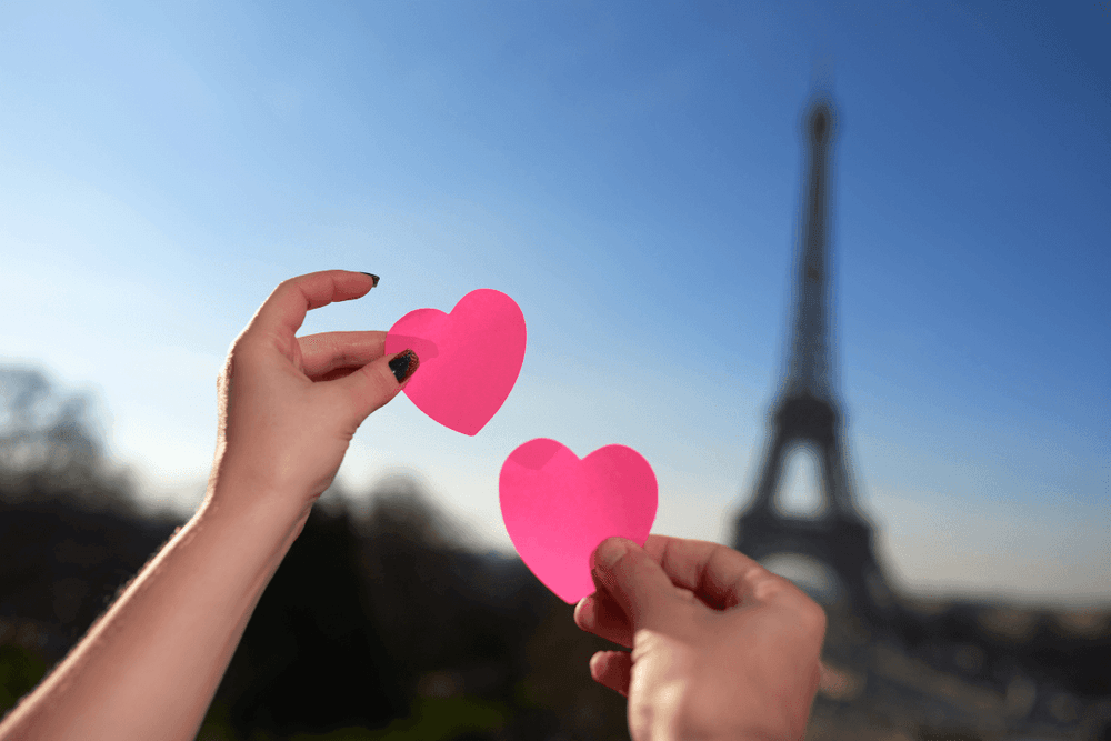 Hands holding paper hearts by the Eiffel Tower under a bright sky near Warwick Paris Champs Elysées
